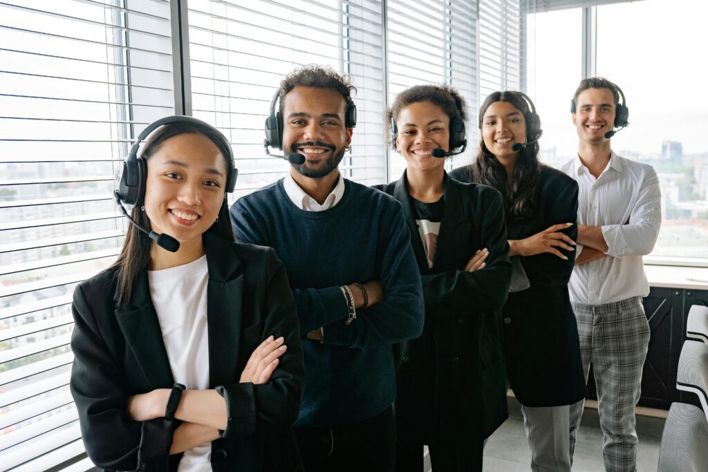 A cheerful, diverse team with headsets posing in a bright office environment.